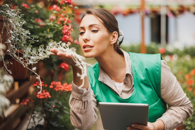 Young entrepreneur woman using digital tablet while checking flowers in a greenhouse.