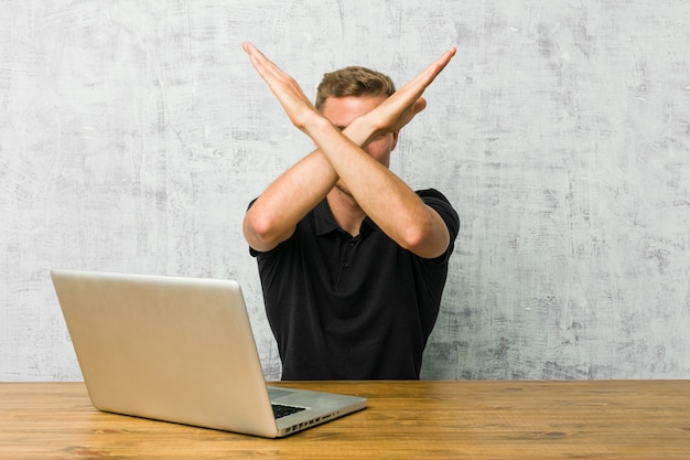 Young entrepreneur working with his laptop on a desk keeping two arms crossed, denial concept.