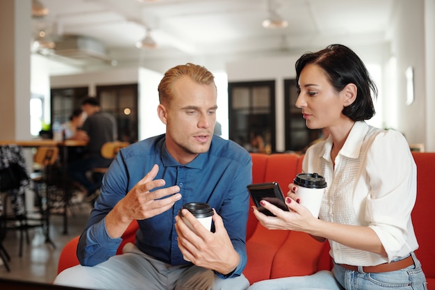 Молодые предприниматели пьют кофе в кафе и выбирают новое мобильное приложение для управления проектами