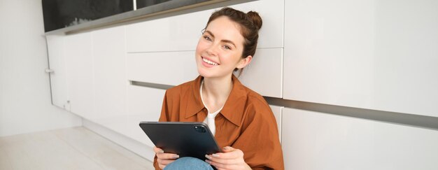 Young entrepreneurs smiling cute woman with digital tablet sitting with gadget on kitchen floor and