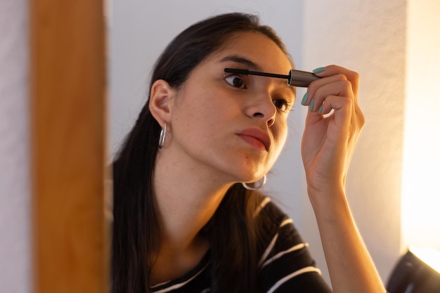Young ethnic lady looking in mirror while applying mascara person