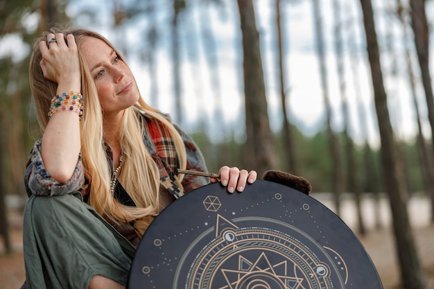 Young ethnic mature shaman female is walking and playing drums meditative music