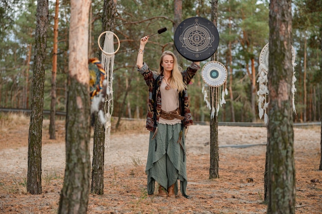 Photo young ethnic mature shaman female is walking and playing drums meditative music