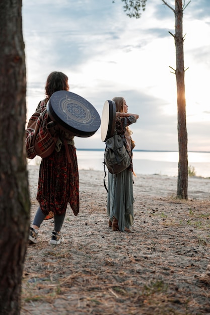 若い民族の成熟したシャーマンの女性が歩き、ドラムの瞑想音楽を演奏している