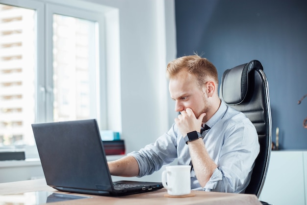 Il giovane uomo d'affari europeo sta lavorando su un laptop in un moderno ufficio luminoso