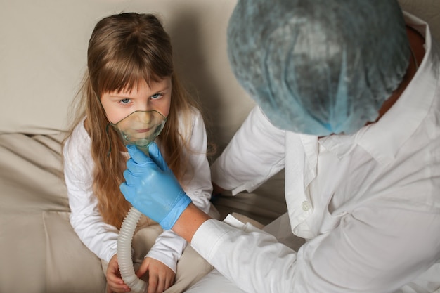 Photo young european doctor helping a little girl with a spray mask doctor applying inhalation medication therapy on little girl with inhalation therapy for asthma with inhaler mask