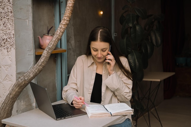 Photo a young european freelancer girl with long dark hair in a shirt and jeans remotely works in a cafe