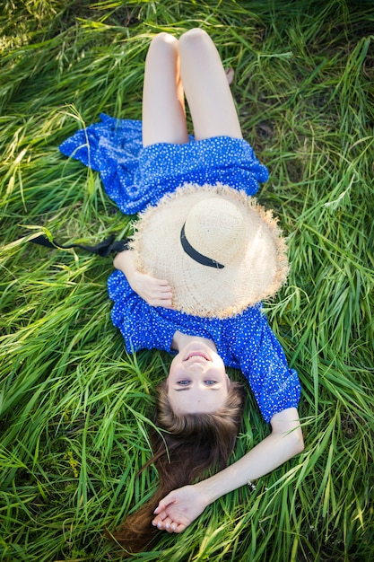 파란 드레스에 젊은 유럽 여자는 모자와 함께 잔디에 놓여