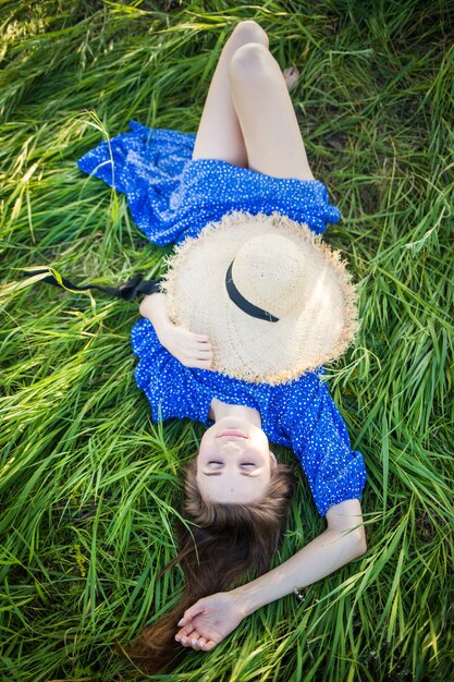 Young european girl in a blue dress lies in the grass with a hat