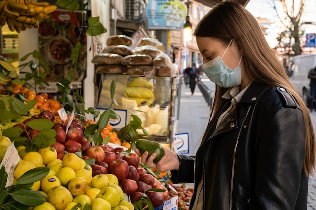 若いヨーロッパの女の子は、保護マスクで市場で新鮮な果物や野菜を購入します