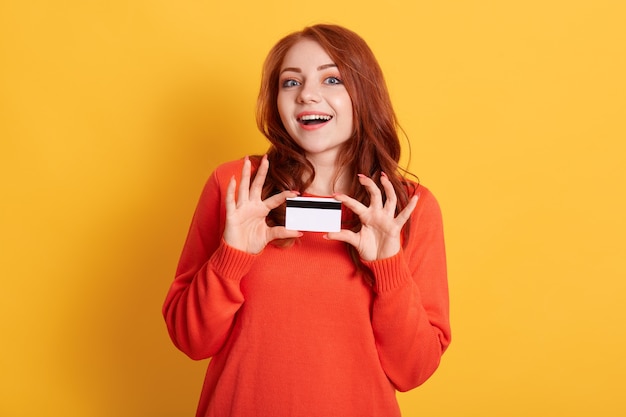 Photo young european girl holding credit card isolated on yellow space