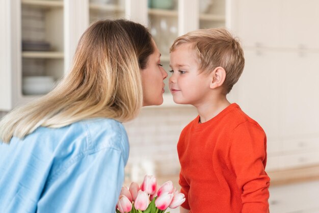 Young european mom kissing her little son for his tulips for\
celebration