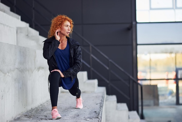 Photo young european redhead woman in sportive clothes doing exercises on stairs outdoors