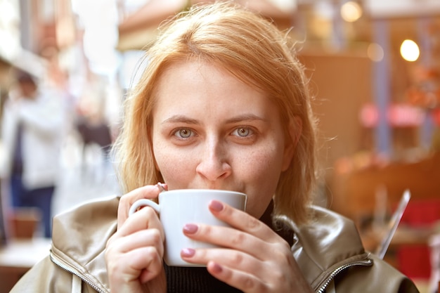 young european woman drinking coffee in street cafe during cold weather.