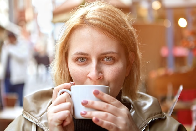 Young European woman drinking coffee in street cafe during cold weather.