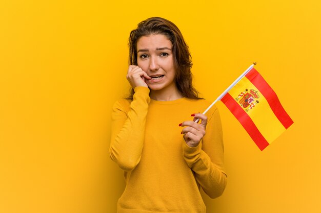 爪をかむスペイン国旗を保持している若いヨーロッパの女性、神経質で非常に心配しています。