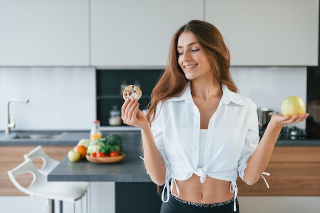 若いヨーロッパの女性は、健康的な食事と一緒に屋内のキッチンで屋内にいます