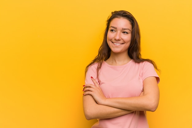 Giovane donna europea isolata su sfondo giallo sorridente fiducioso con le braccia incrociate.