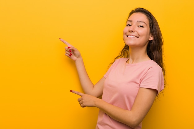 Молодая европейская женщина изолированная над желтым возбужденным указывать с указательными пальцами прочь.