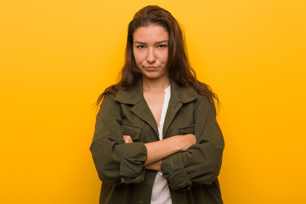 Young european woman isolated over yellow frowning her face in displeasure, keeps arms folded.