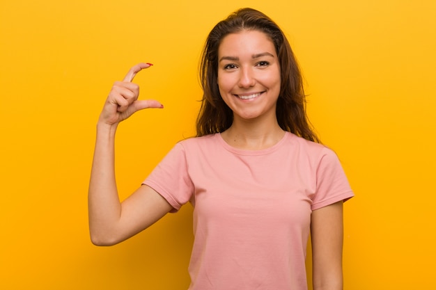 Giovane donna europea isolata sopra la tenuta gialla qualcosa di piccolo con gli indici, sorridente e sicuro.