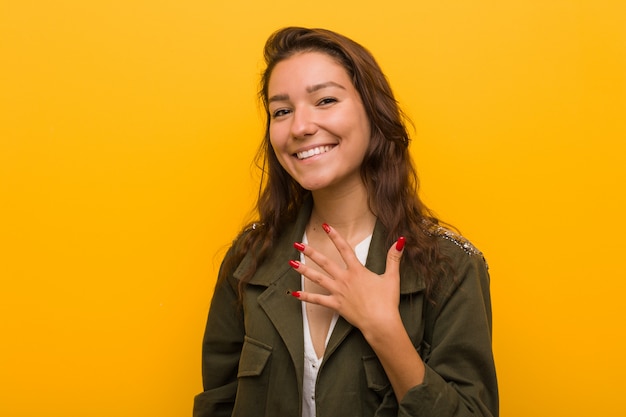 Foto la giovane donna europea isolata sopra giallo ride ad alta voce tenendo la mano sul petto.