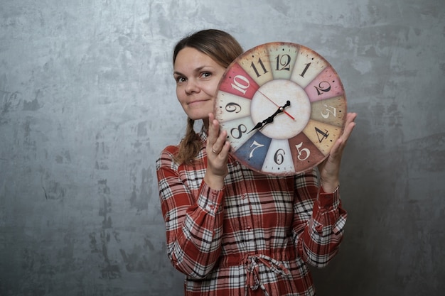 Photo young european woman in a plaid dress holding in his hand a round vintage clock