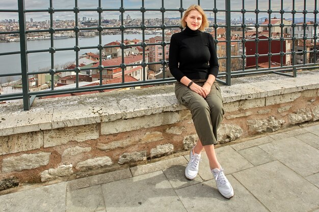 Young European woman poses against backdrop of cityscape while walking around Istanbul.