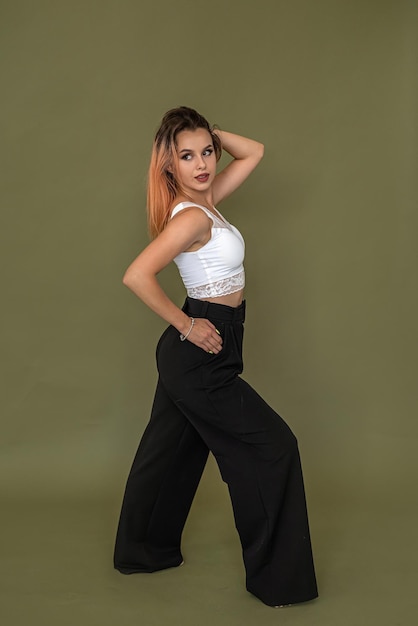 Young european woman in stylish white top and black pants posing in full growth isolated on green background fashion style concept