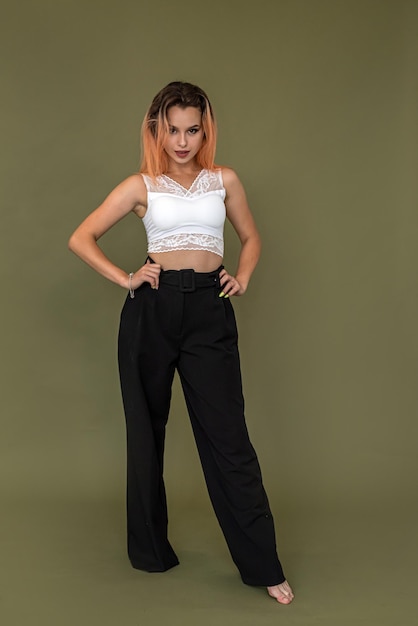 Young european woman in stylish white top and black pants posing in full growth isolated on green background fashion style concept