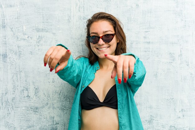 Young european woman wearing bikini cheerful smiles pointing to front.