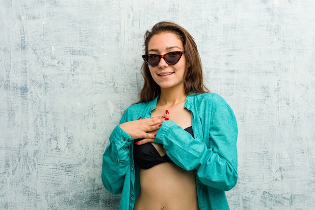 Young european woman wearing bikini has friendly expression, pressing palm to chest. Love .