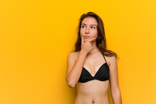 Young european woman wearing bikini looking sideways with doubtful and skeptical expression.