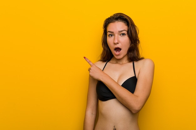 Young european woman wearing bikini pointing to the side