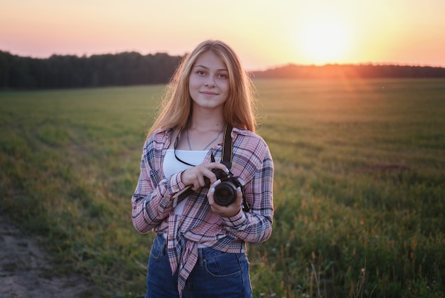 Young European woman with a camera in the summer evening at sunset taking pictures