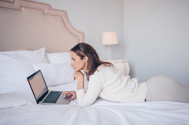 Young european woman working on a laptop in white bedroom