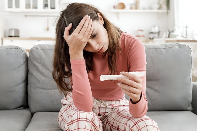Young European woman worried because she has got positive results of pregnancy test sitting alone at home