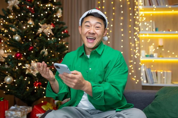 Young excited asian man happy positive smile rejoice celebrate victory phone xmas winter sitting at