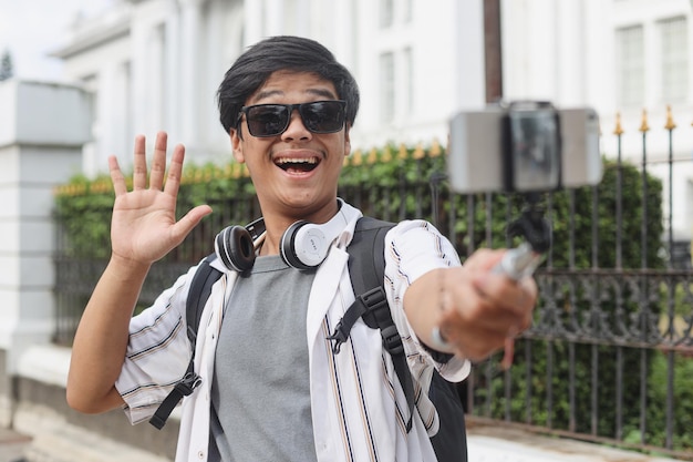 Young excited Asian man wearing sunglasses and backpack taking a video vlog