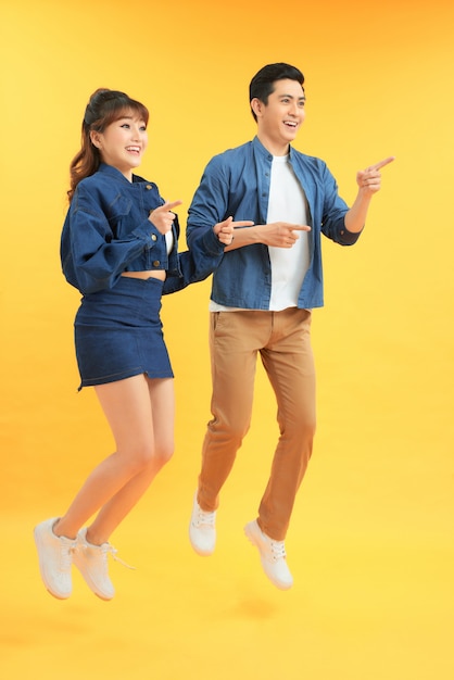 Young excited asian people man and woman jumping isolated over yellow background