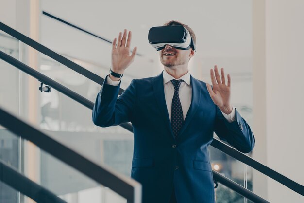 VRヘッドセットを使用してオフィスのインテリアに立っているフォーマルな服装で若い興奮したヨーロッパのビジネスマン