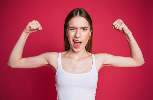 Young excited and happy woman with surprised face looks on camera over pink wall