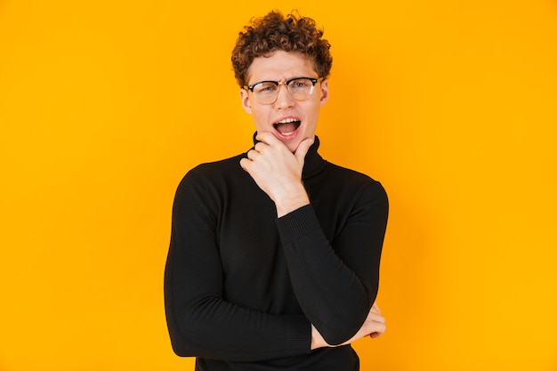 young excited man in eyeglasses poising isolated on yellow