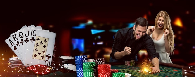 Young excited man and woman are happy about their win. They are posing while standing at playing table against colorful background. Winning combination in poker, stacks of chips. Gambling, casino