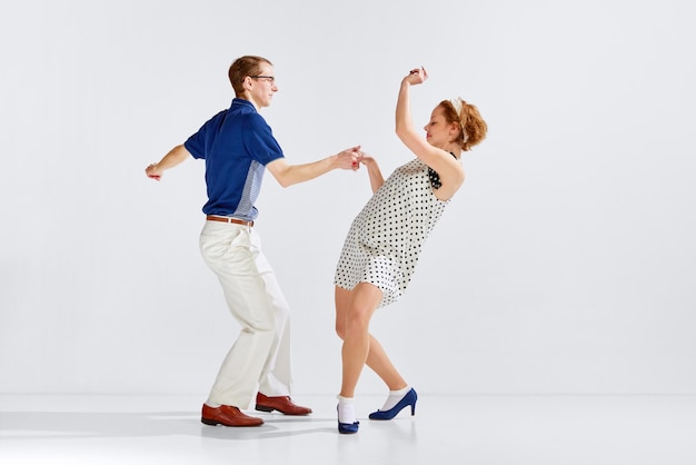 Молодой взволнованный мужчина и женщина в стильной одежде танцуют ретро-танец изолированы на белом