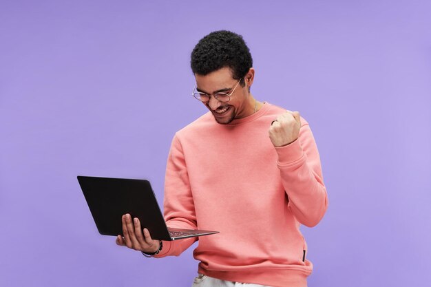 Young excited programmer in eyeglasses and pink pullover expressing joy