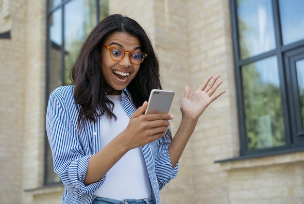 Giovane donna eccitata utilizzando il telefono cellulare che compera online