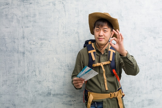 확인 제스처를 하 고 쾌활하고 자신감 항공 티켓을 들고 젊은 탐험가 중국 남자