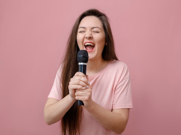 Young expressive woman with microphone in hand on pink background