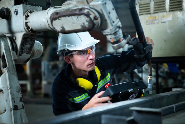 Молодой фабричный рабочий, работающий с искусной роботизированной рукой